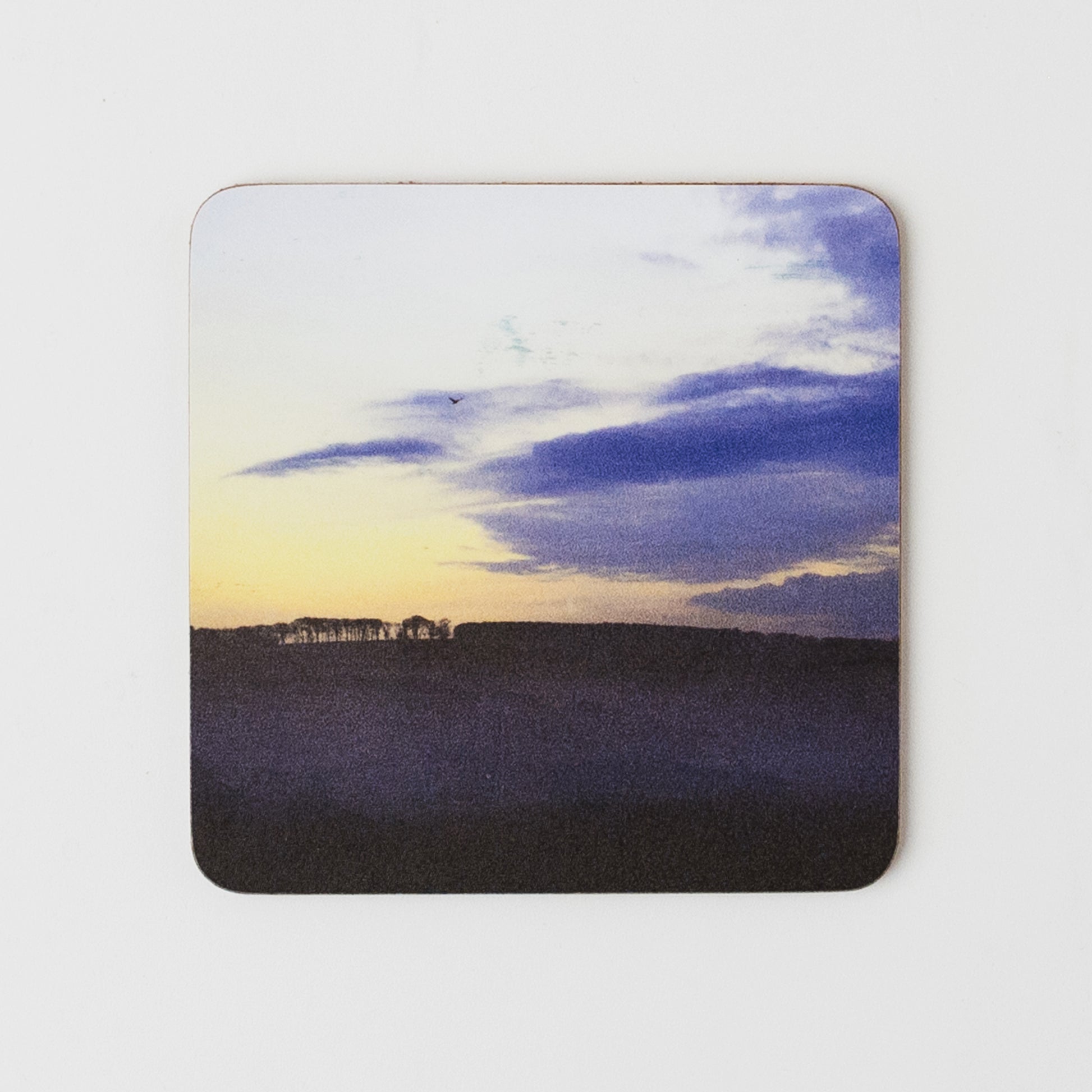 Coaster with a landscape design of a sunset over a field on a white background